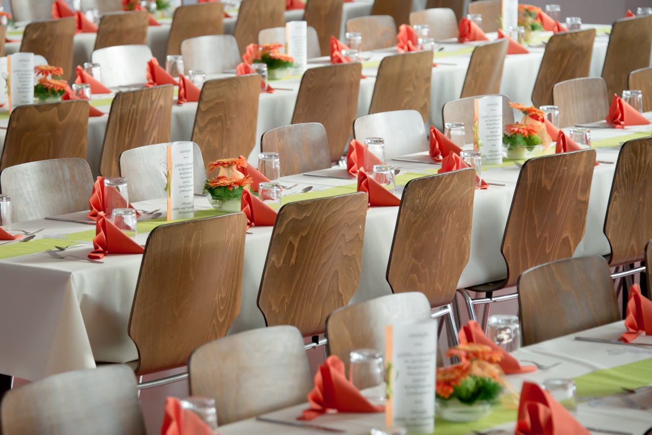 Services Beautifully arranged tables with wooden chairs for a formal event, adorned with orange flowers.