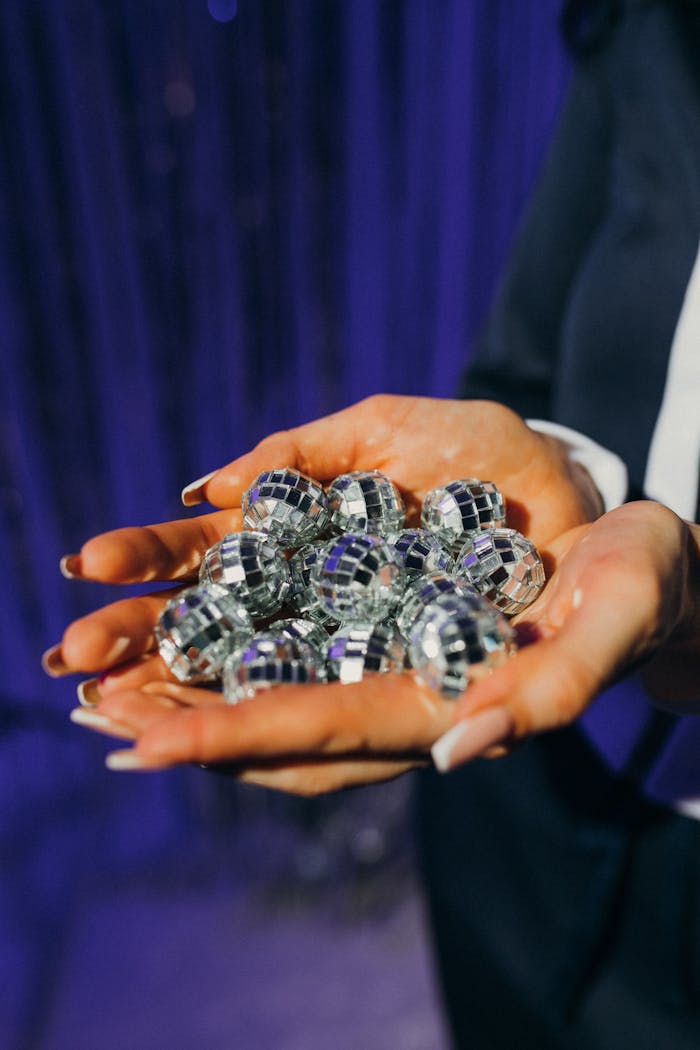 A close-up shot of hands holding mini disco balls against a purple background, ideal for party themes.